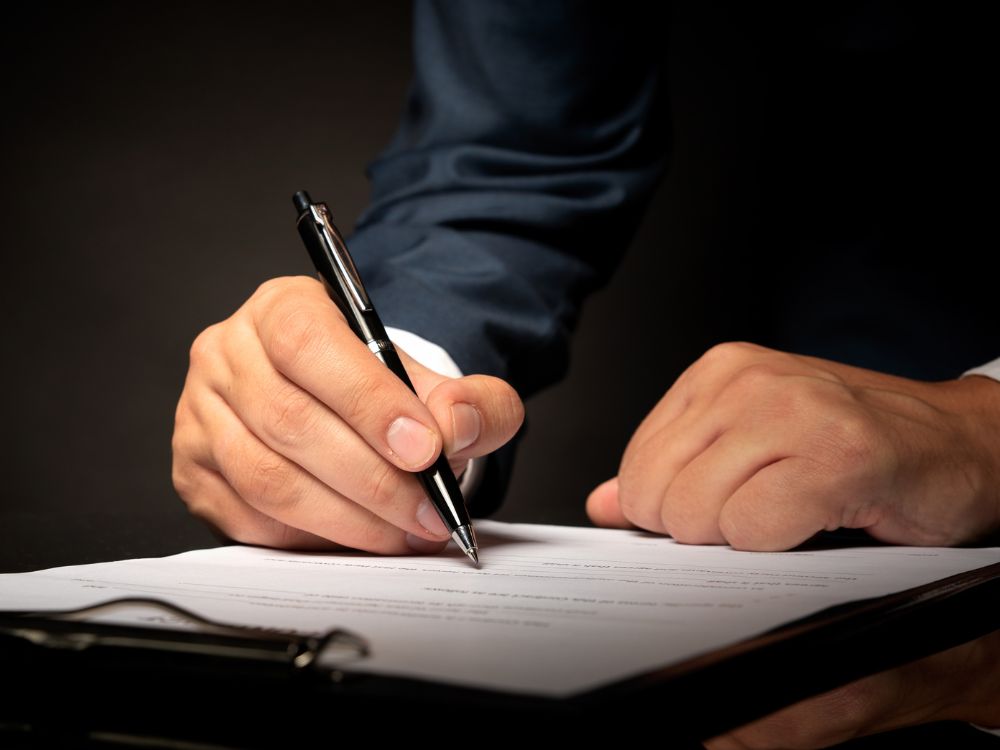 Pessoa assinando documento jurídico sobre mesa de escritório, representando a importância da documentação correta na averbação da construção.