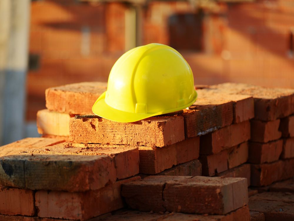 Capacete de segurança apoiado em tijolos simbolizando o fim da obra e o início do processo de averbação da construção no cartório de imóveis.
