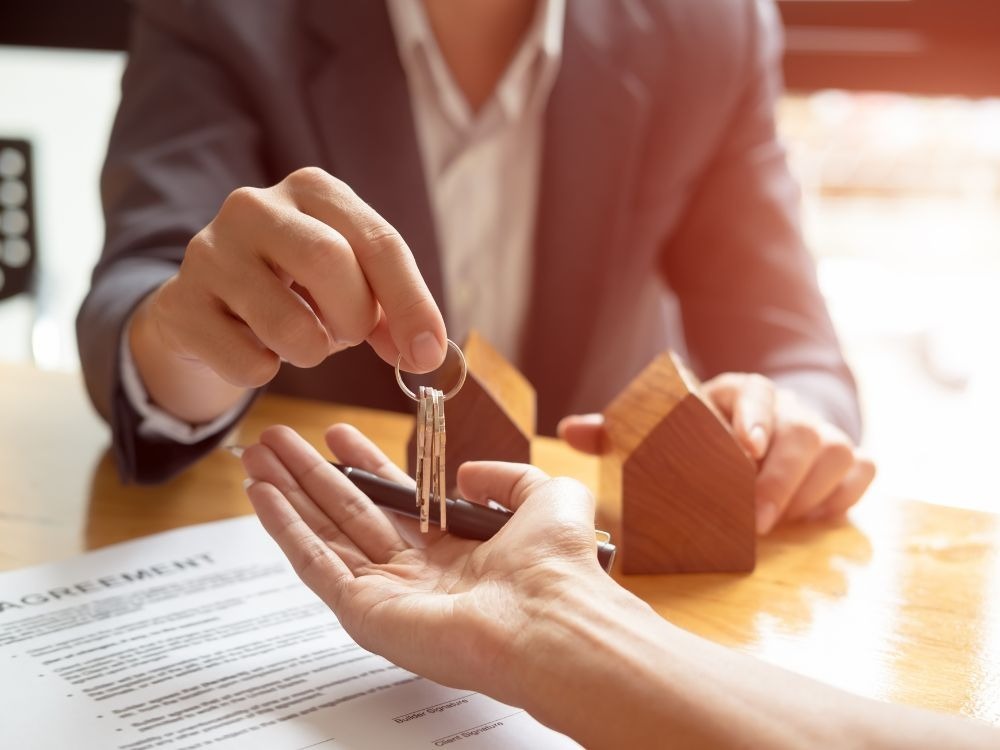Corretor realizando a entrega das chaves de um apartamento comprado na planta durante aperto de mãos entre comprador e vendedor.