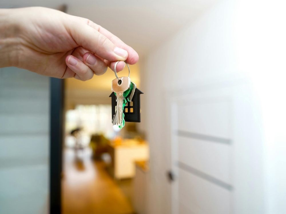 Mão segurando chave com chaveiro de casa simbolizando a entrega das chaves de um apartamento comprado na planta ao novo morador.