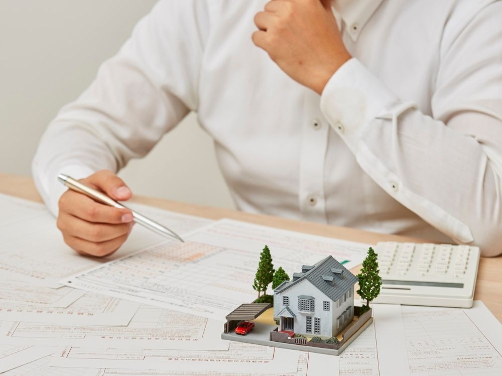 Pessoa analisando dados financeiros com maquete de casa refletindo se investimento imobiliário vale a pena.