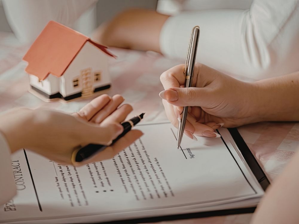Assinatura de contrato com miniatura de imóvel representando quando investimento imobiliário vale a pena.