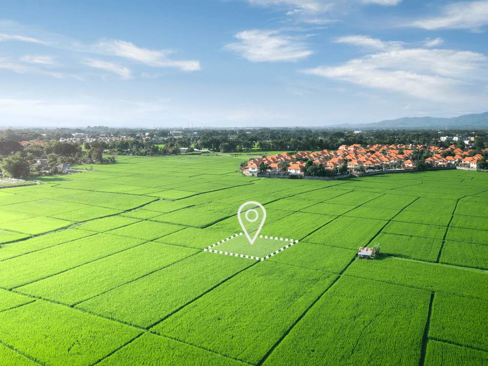 Vista aérea de um terreno demarcado por marcador de localização em área rural, ilustrando como saber se um terreno tem dono