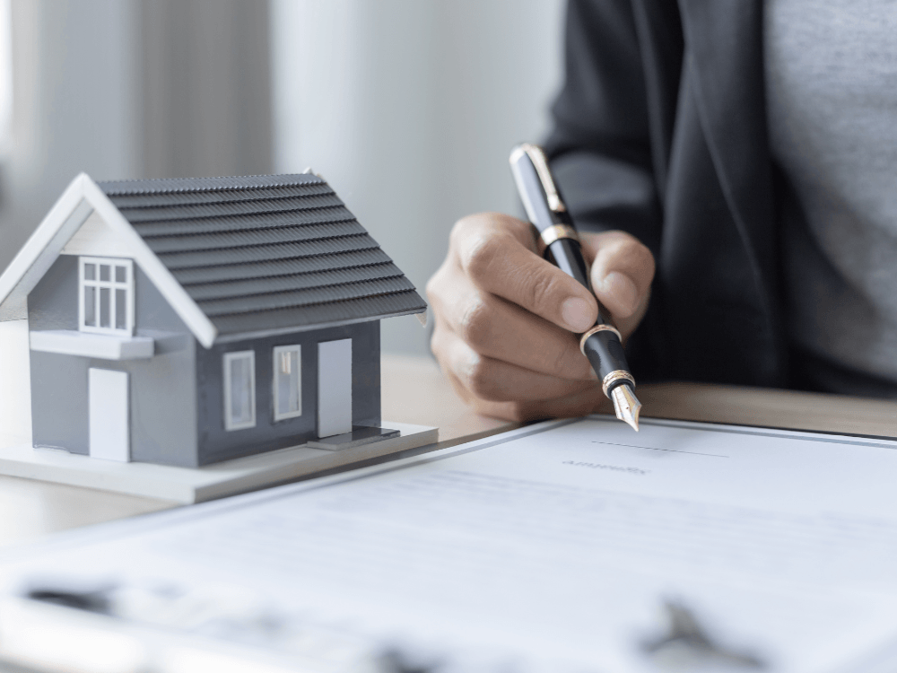Pessoa assinando documentos ao lado de uma maquete residencial durante o processo para saber se é possível vender um imóvel financiado.