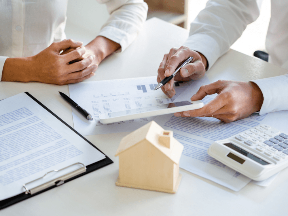 Pessoas analisam documentos, tablet e calculadora durante conferência de informações após o registro oficial de um imóvel. Tudo para explicar sobre após o registro do imóvel qual o próximo passo.