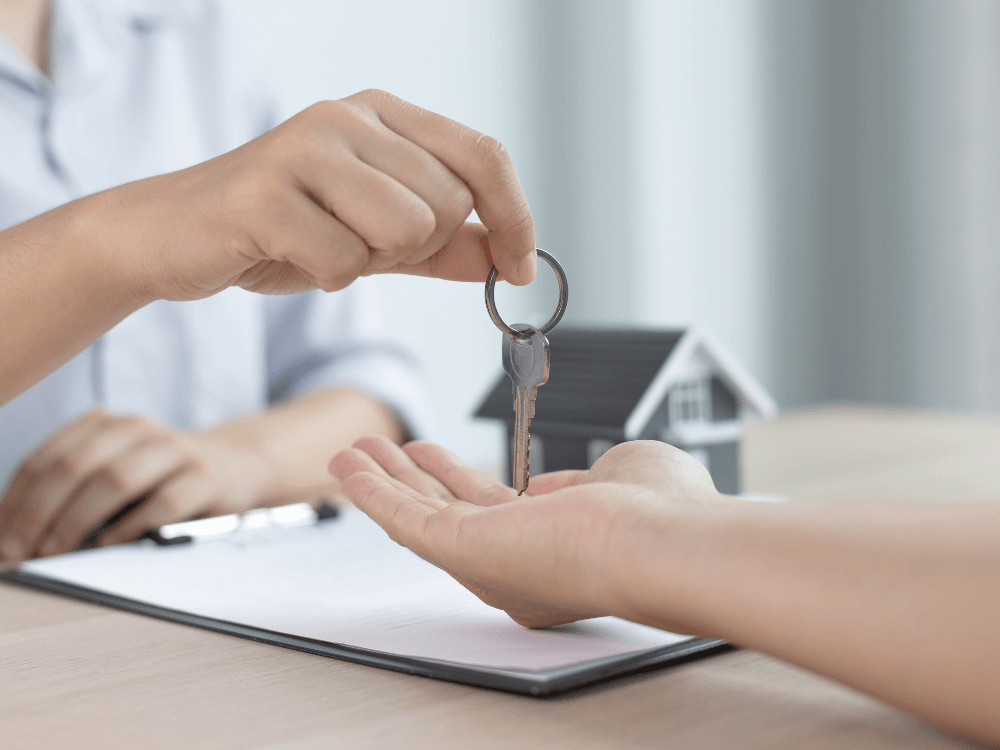 Pessoa entrega uma chave ao futuro proprietário sobre uma mesa de atendimento, simbolizando a negociação de um imóvel avaliado.