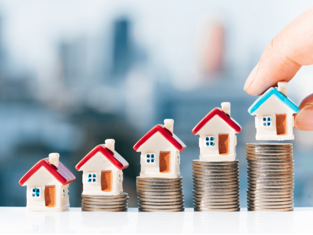 Miniaturas de casas sobre pilhas crescentes de moedas representam a valorização e o investimento em imóveis.