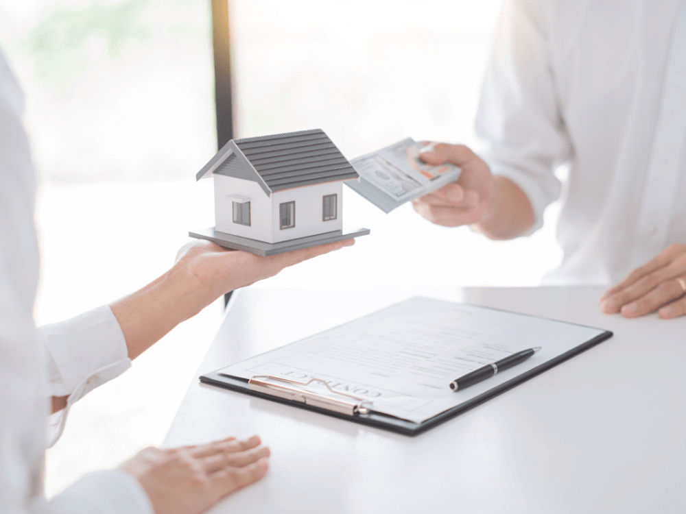 Miniatura de uma casa é apresentada durante uma negociação imobiliária com documentos sobre a mesa.