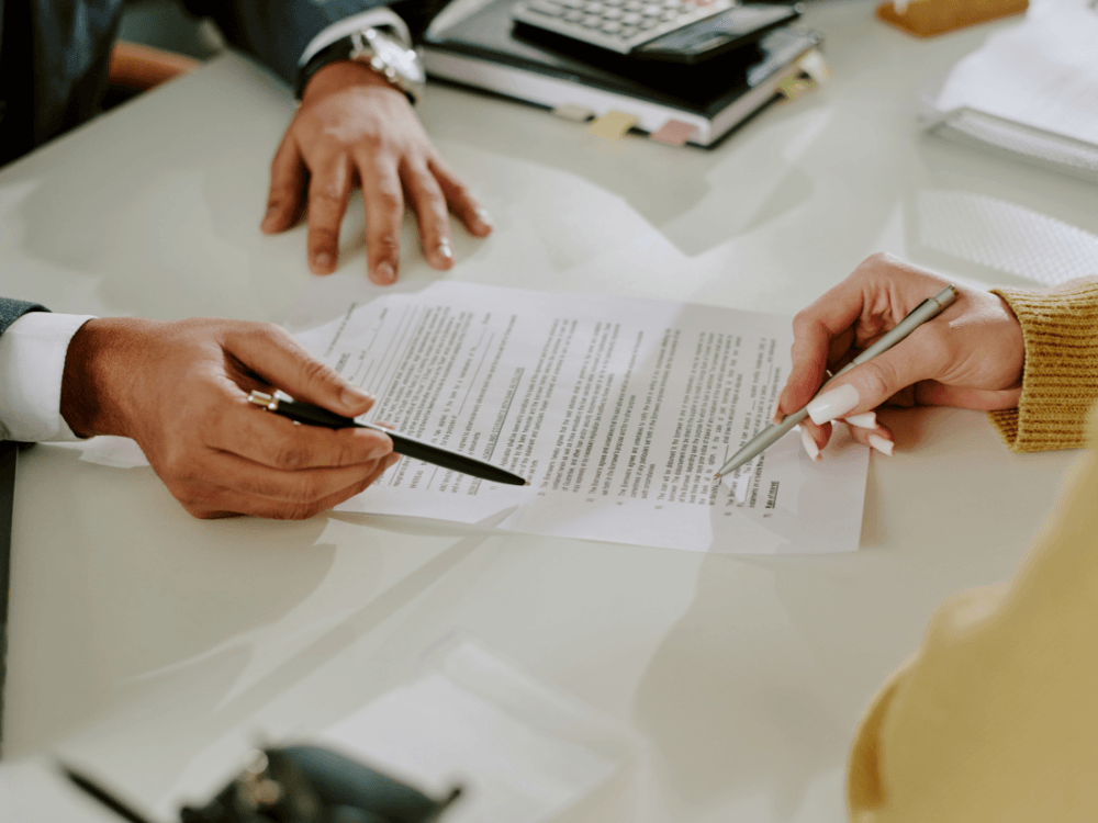 Pessoas analisam e assinam um documento imobiliário, representando a formalização de uma negociação de propriedade. Tudo para explicar a diferença entre escritura e registro.