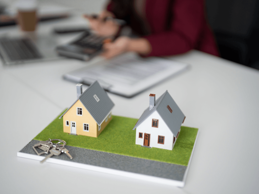 Duas maquetes de casas lado a lado sobre uma representação de terreno, com chaves próximas às propriedades.