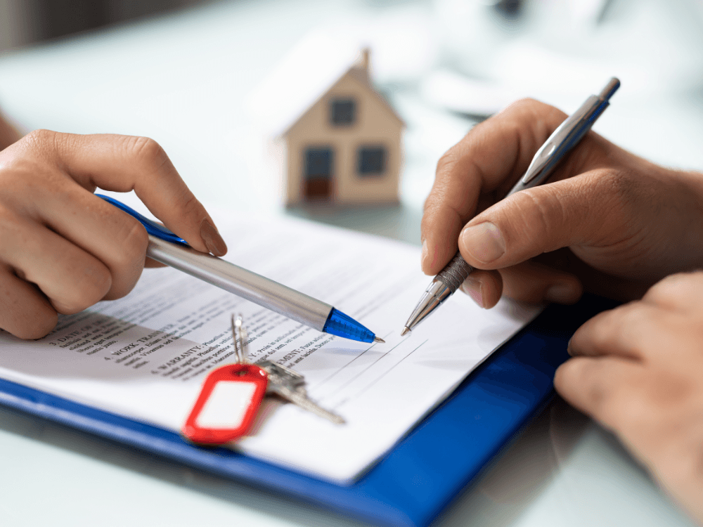 Duas pessoas analisam e assinam documentos imobiliários com chaves sobre a mesa durante a formalização de um imóvel.