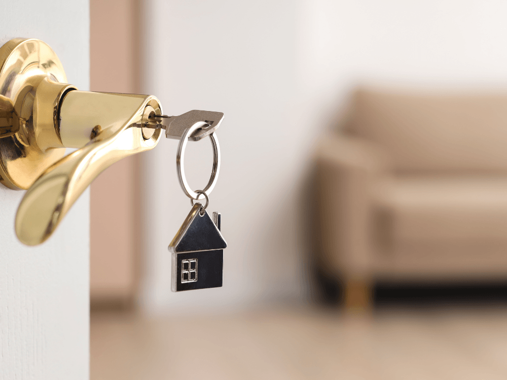 Chave com pequeno chaveiro em formato de casa na fechadura de uma porta, representando o acesso ao imóvel alugado. Tudo para explicar se o proprietário pode pedir imóvel alugado