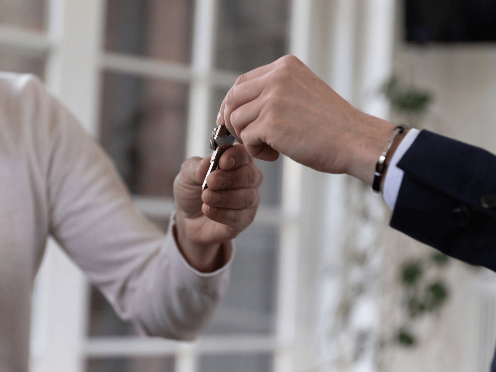 Duas pessoas realizam a entrega de uma chave durante uma negociação imobiliária, simbolizando a chegada ao novo apartamento.