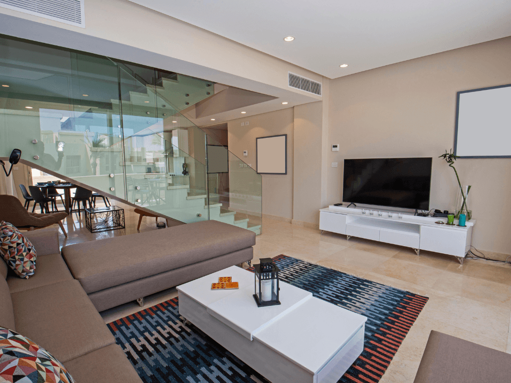 Sala de apartamento duplex com sofá, televisão e escada de vidro que conecta os dois pavimentos da residência