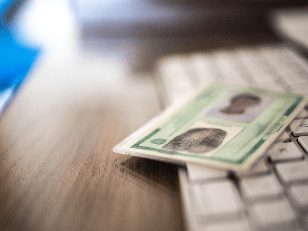 Documento de identificação com fotografia sobre uma mesa, ao lado de um teclado, representando a conferência cadastral para alugar um imóvel.